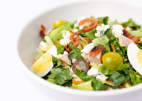 A fresh salad with greens, cherry tomatoes, bacon, hard-boiled egg, and blue cheese in a white bowl.