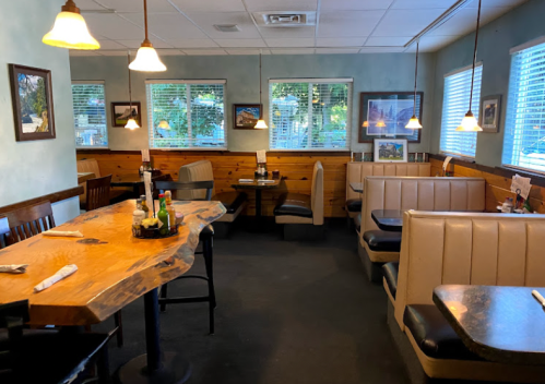 Cozy restaurant interior with wooden tables, booths, and large windows letting in natural light.