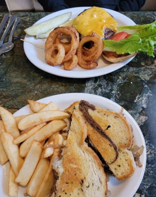 A plate with a cheeseburger, onion rings, and pickles; another plate with a sandwich and fries.