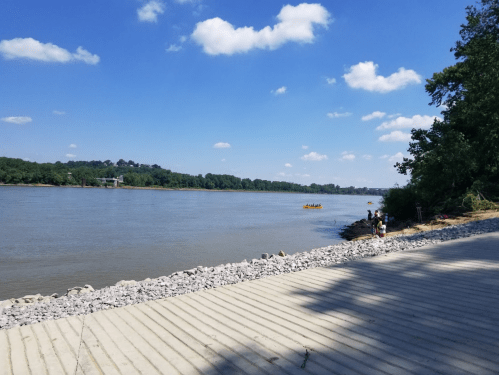A serene river scene with a clear blue sky, trees lining the shore, and a small boat in the distance.
