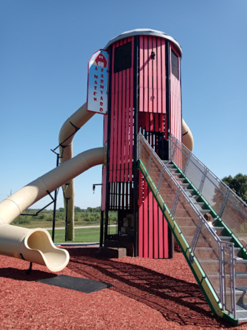 Colorful playground structure with a tall slide, stairs, and a tower, set in a grassy area under a clear blue sky.
