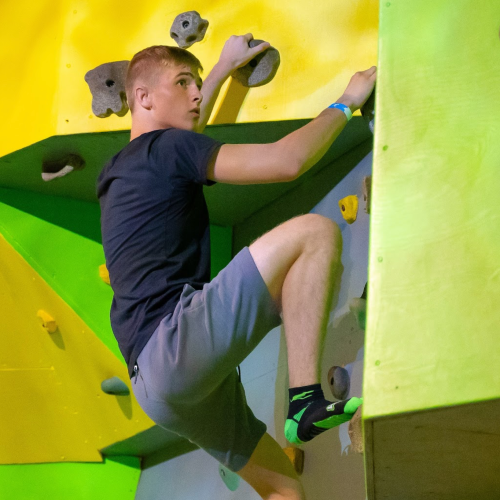 A young climber ascends a colorful indoor climbing wall, focused and determined.