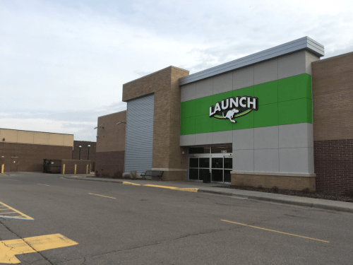 Exterior of a building with a green "LAUNCH" sign, featuring a large entrance and a parking lot in front.
