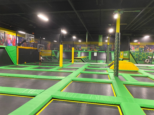 A spacious indoor trampoline park with green and black trampolines, basketball hoops, and a vibrant atmosphere.