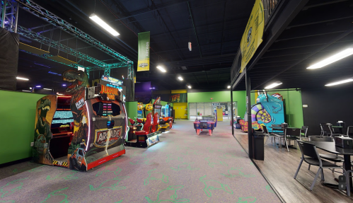 A vibrant arcade with colorful games, seating areas, and green walls, creating a fun and lively atmosphere.