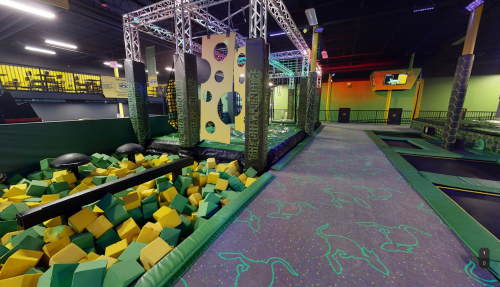 A vibrant indoor trampoline park featuring a foam pit and colorful flooring, with various play areas and equipment.