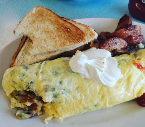 A plate with a fluffy omelette filled with vegetables, served with toast and seasoned potato wedges.