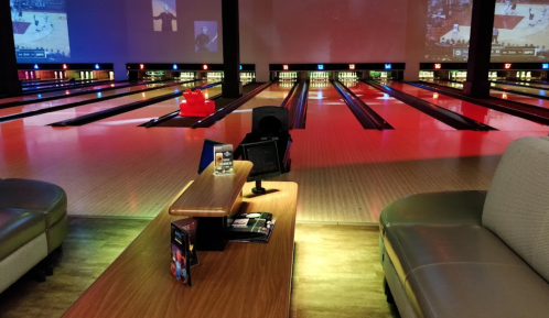 A bowling alley with colorful lights, empty lanes, and a seating area with a table and drinks.