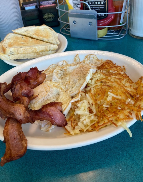 A plate of breakfast featuring crispy bacon, fried eggs, and golden hash browns, with toast in the background.