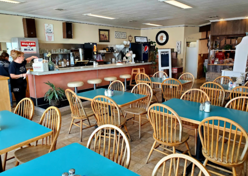 A cozy diner interior with wooden tables, a counter, and a staff member serving customers.