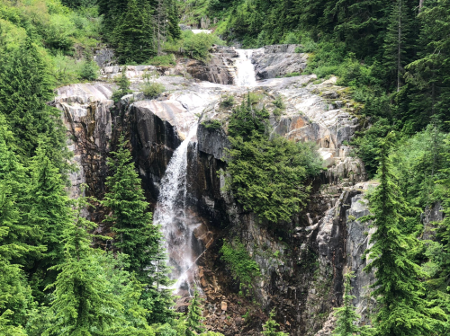 A scenic waterfall cascading down rocky cliffs, surrounded by lush green trees and dense forest.