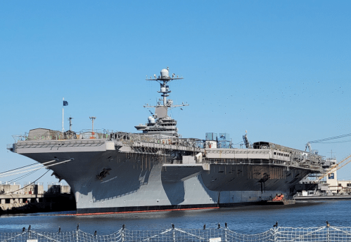 A large aircraft carrier docked in a harbor under a clear blue sky.