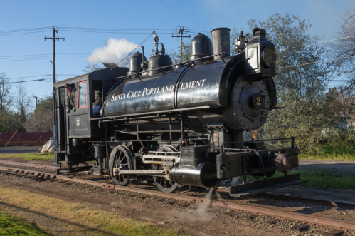 A vintage steam locomotive with black exterior, labeled "Santa Cruz Portland Cement," on a railway track.