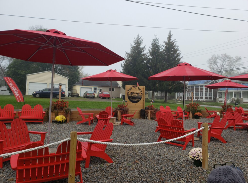 A cozy outdoor seating area with red Adirondack chairs and umbrellas, surrounded by gravel and autumn flowers.