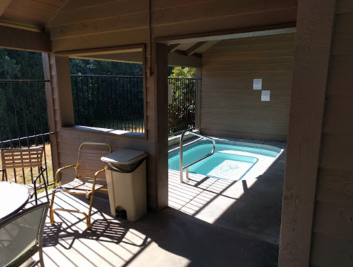 A small indoor pool area with a railing, chairs, and a trash can, surrounded by wooden walls and windows.
