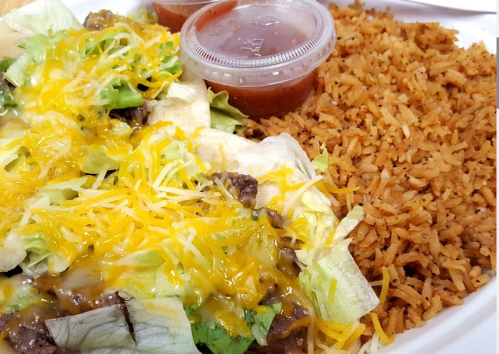 A plate of rice with seasoned beef, lettuce, and melted cheese, accompanied by two cups of salsa.