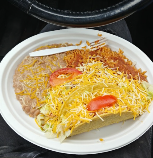 A plate of food featuring tacos with lettuce and tomato, rice, and refried beans, with a plastic fork on the side.