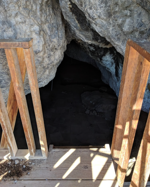 A wooden staircase leads into a dark cave entrance surrounded by large rocks.
