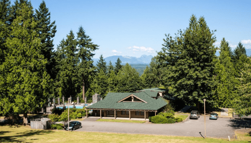 A scenic view of a building surrounded by trees, with mountains in the background and a clear blue sky.