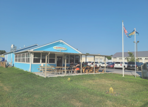 A blue restaurant with outdoor seating, flags flying, and patrons enjoying their meals on a sunny day.