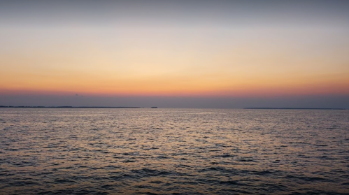 A serene ocean view at sunset, with soft hues of orange and purple reflecting on the calm water.