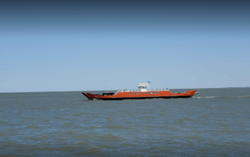 An orange ferry boat navigating through calm waters under a clear blue sky.