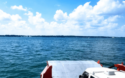 A view of calm blue water with a cloudy sky, featuring a ferry's bow in the foreground.