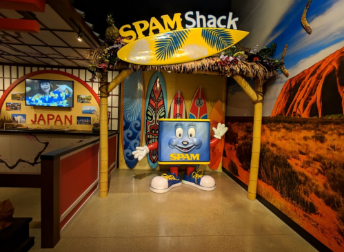 A colorful SPAM Shack entrance featuring a cartoon SPAM character and surfboards, set against a vibrant mural.