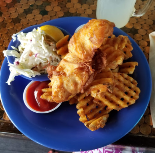 A blue plate with fried fish, waffle fries, coleslaw, and dipping sauce on a wooden table.