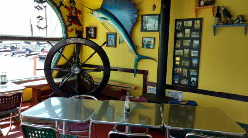 Colorful cafe interior with nautical decor, including a ship's wheel and fish artwork, and tables set for dining.