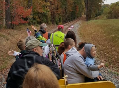 A group of people on a train ride through a colorful forest, waving flags and enjoying the scenery.