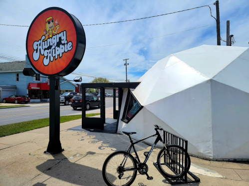 A black bicycle parked near the entrance of the Hungry Hippie restaurant, featuring a round sign and a unique geometric building.