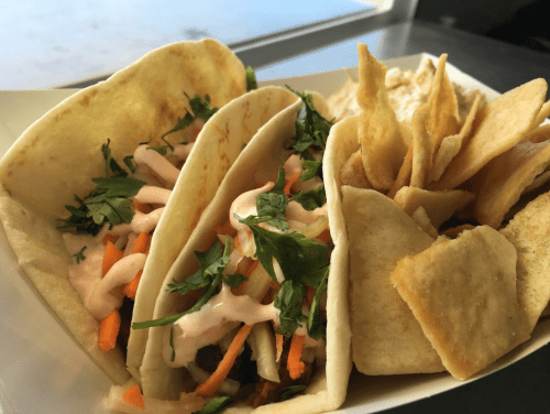 Three tacos filled with vegetables and sauce, served with a side of crispy tortilla chips.