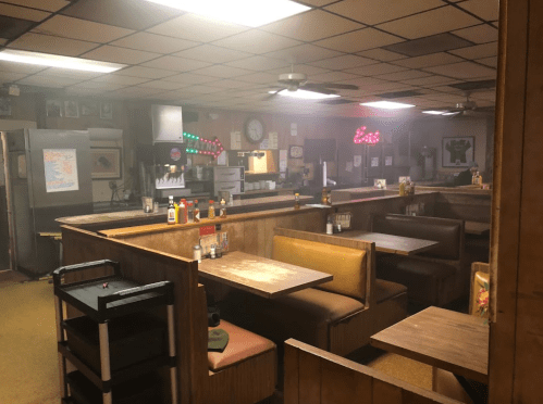 A dimly lit diner interior with booths, a counter, and a foggy atmosphere, featuring various condiments on tables.