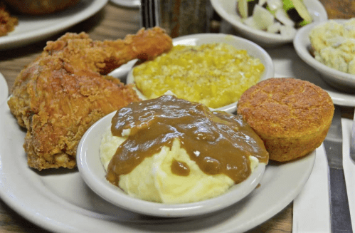 A plate of fried chicken, mashed potatoes with gravy, cornbread, and a side of corn.