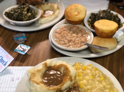 Two plates of Southern comfort food featuring greens, cornbread, mashed potatoes with gravy, and baked beans.