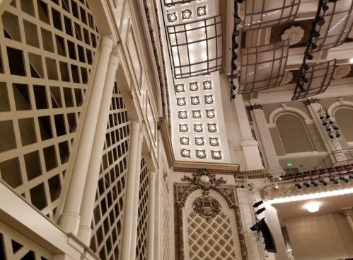 Interior view of a grand theater, showcasing ornate architectural details and decorative lighting.