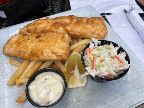 Two pieces of golden fried fish with fries, coleslaw, a lemon wedge, and tartar sauce on a plate.