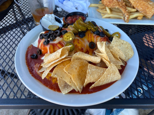 A plate of nachos topped with cheese, jalapeños, olives, and served with salsa and tortilla chips on the side.