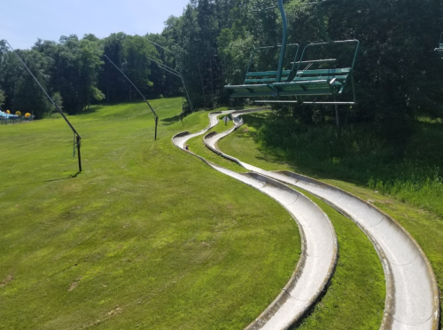 A winding summer slide path alongside a ski lift in a green, grassy landscape.