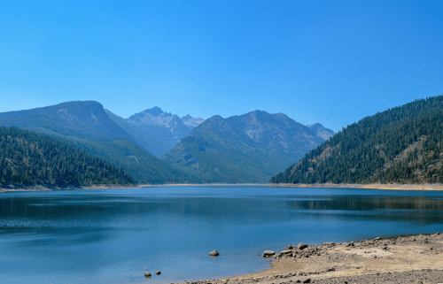 A serene lake surrounded by mountains and lush forests under a clear blue sky.