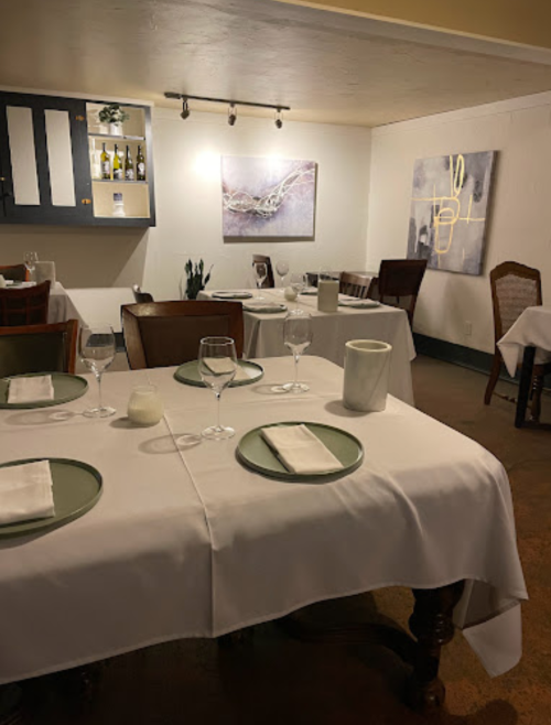 A cozy restaurant interior with elegantly set tables, white tablecloths, and modern artwork on the walls.