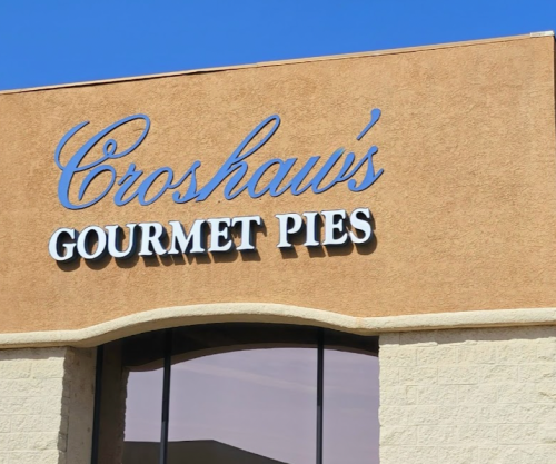 Sign for "Croshaw's Gourmet Pies" on a building with a clear blue sky in the background.