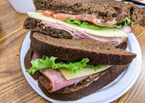A stacked sandwich on a plate, featuring layers of ham, cheese, and lettuce between slices of dark rye bread.
