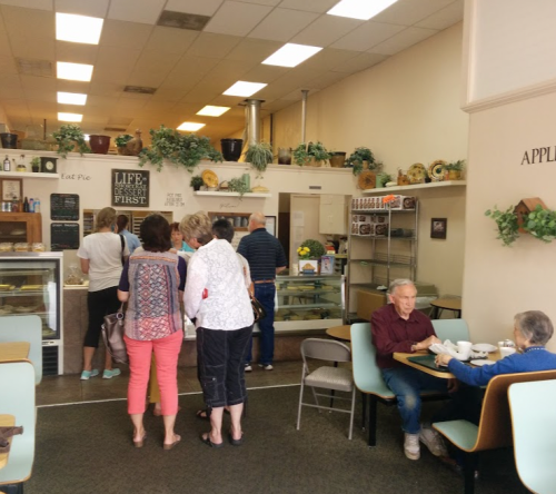 A cozy café interior with customers in line and others seated at tables, enjoying desserts and conversation.
