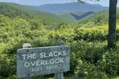 A scenic view from The Slacks Overlook sign, showcasing lush green mountains and valleys at an elevation of 2800 feet.