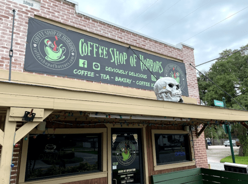 Exterior of Coffee Shop of Horrors featuring a skull decoration and a sign promoting coffee, tea, and baked goods.
