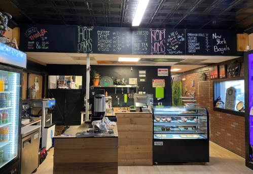 Interior of a café featuring a menu board, display case with baked goods, and a coffee station. Cozy atmosphere.