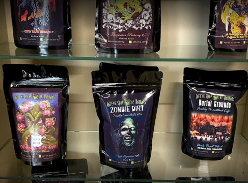 Three colorful coffee bags labeled "Zombie Dirt," "Burial Grounds," and "Creepy Coffee," displayed on a shelf.