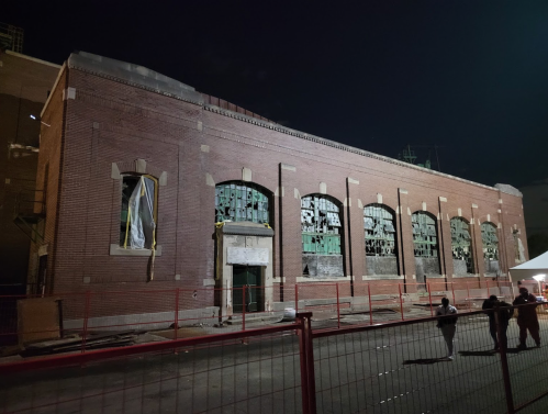 Abandoned brick building at night, featuring broken windows and a fenced-off area.